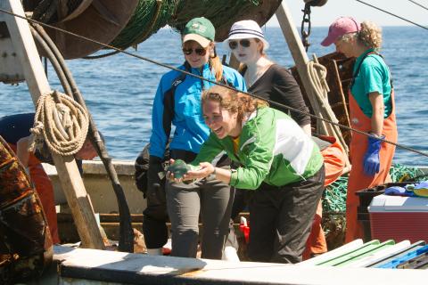 a group of students on a fishing boat, with one holding a fish and smiling