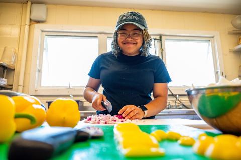 a woman wearing hat, chopping onions and peppers. Smiling