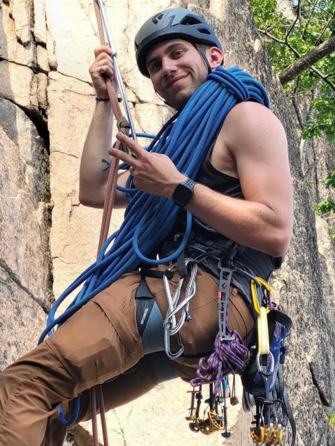 man in helmet rock climbing, tethered to rope