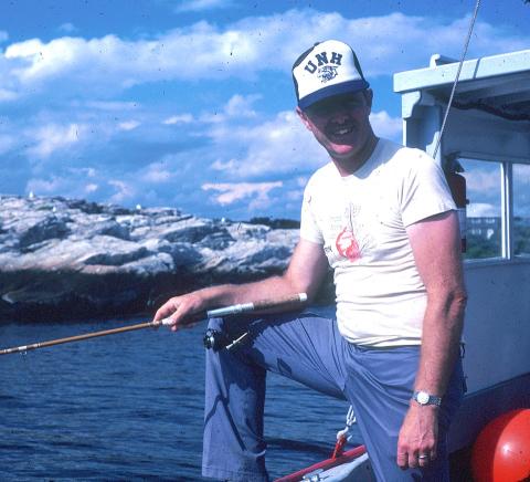 man in UNH hat on boat with fishing pole
