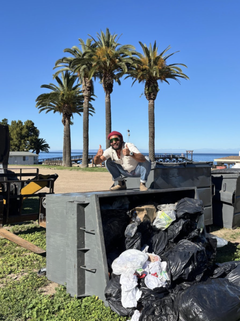 man squatting on top of an overturned dumpster, thumbs up