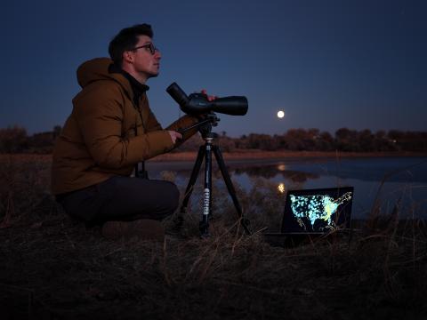 a man looking into night sky with scope